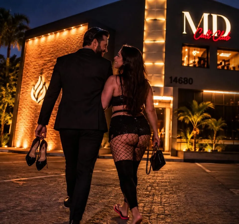 Um casal caminha de mãos dadas até a fachada iluminada da MD Cult Club. Ele, de terno, carrega os sapatos de salto dela; ela segue de chinelo.